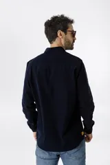 Camisa de pana color azul marino, con mangas largas, cuello clásico y dos bolsillos frontales con solapa y botón.