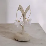 Aros colgantes con diseño de flores blancas de resina y centro de perla, montados sobre gancho de metal dorado.