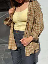 Camisa escocesa holgada, de manga larga, con estampa de cuadros en tonos de verde y marrón, y cierre frontal con botones.