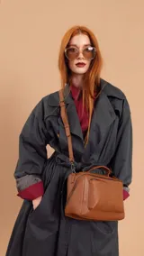 Bandolera de diseño estructurado en color suela, con asa superior fija y correa larga ajustable y extraíble. Presenta un bolsillo frontal con cierre y un compartimento principal con cierre cruzado.