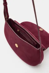 Bolso bandolera de piel de ante color bordó, con solapa curva, cierre de clip metálico y correa larga ajustable.