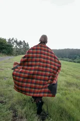 Capa oversize de corte amplio con estampado de cuadros en tonos rojos, negros y marrones. Presenta cuello alto, cierre frontal con botones, bolsillos delanteros y mangas ajustables mediante trabillas con botones.