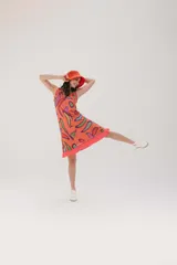 Vestido corto naranja con estampado abstracto en tonos morado, verde y blanco. Tiene corte recto, cuello redondo y mangas cortas.