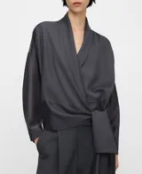 Blusa gris de corte cruzado tipo cache-coeur, con escote en V, mangas largas y detalle de lazo para atar en el lateral de la cintura. Confeccionada en mezcla de liocel y poliéster.