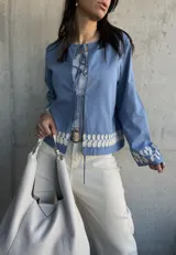 Chaqueta celeste con bordados florales blancos en el ruedo y los puños, con escote redondo y lazos para atar en el frente.