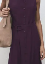 Vestido midi color borravino, sin mangas, con cuello camisero, cierre frontal con botones y cinturón ajustable del mismo tejido.