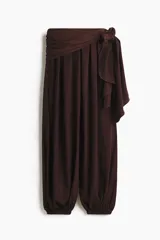 Pantalón de tiro alto color bordó con leve brillo, cintura cruzada con detalle de lazo lateral y piernas estilo globo con elásticos en los tobillos.