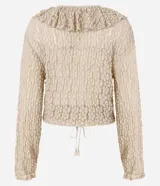 Blusa tipo bata de encaje texturizado color beige, con escote en V, mangas largas y volados aplicados en el escote. Presenta cierre frontal con botones y lazo de ajuste en la cintura.