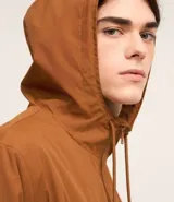 Campera rompevientos color verde oliva con capucha ajustable con cordón, cierre frontal con cremallera, bolsillos laterales con cremallera, puños con elástico y forro interior. Ligera y versátil, ideal para proteger del viento y la lluvia ligera.