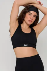 Conjunto deportivo de tres piezas en color negro, compuesto por un top de manga larga con cuello redondo y logo estampado, un top de bretel ancho y una calza chupín de tiro alto. El diseño presenta detalles de tejido con textura en zonas estratégicas.