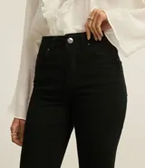 Pantalón negro de sarga con corte flare, tiro alto y cierre frontal con botón y cremallera. Presenta bolsillos delanteros y traseros.