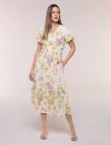 Vestido maxi de gasa color beige con estampado floral en tonos amarillos y rosados, escote en V cruzado, mangas cortas abullonadas y cintura elastizada con nido de abeja.