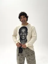 Remera de manga larga color beige con estampado fotográfico frontal de Ronaldinho en blanco y negro. Presenta un corte oversize y cuello redondo.