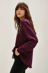Camisa de viscosa color violeta con cuello clásico, manga larga y cierre frontal con botones. Presenta un diseño bordado con lentejuelas doradas en ambos lados del pecho.