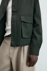 Cazadora relaxed fit color verde oscuro, confeccionada en tejido de algodón. Cuenta con cuello solapa, manga larga con puño abotonado, bolsillos plastrón con solapa en la cadera y cierre frontal de botonadura.