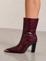 Bota de caña media en cuero vacuno con textura de reptil, color bordó. Presenta punta fina con puntera metálica dorada y taco cuadrado alto de color negro. Incluye cierre lateral interno.