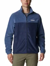 Campera polar Columbia con cierre frontal completo, cuello alto y bolsillos laterales con cierre. Presenta un diseño de bloques de color en dos tonos de azul y el logo de la marca bordado en el pecho.