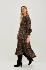 Vestido midi de corte fluido con estampado paisley en tonos oscuros, ocres y rosados. Presenta cuello redondo con lazo de ajuste, mangas largas abullonadas con puños elásticos y falda con volados en el ruedo.