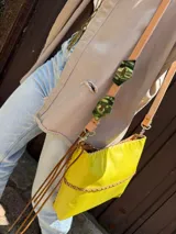Cartera bandolera de cuero flexible color amarillo, con trenza artesanal al frente, interior forrado y correa larga con herrajes de metal.