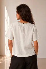 Blusa de lino color beige, de manga corta y cuello redondo, con detalles de bordados geométricos en contraste.