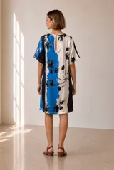 Vestido corto de corte recto y holgado, con mangas cortas y cuello redondo. Presenta un diseño estampado con bloques de color en tonos azul, blanco y negro, con detalles florales.