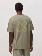 Camiseta de corte oversize color verde oliva, confeccionada en algodón orgánico. Presenta un diseño gráfico de una cruz grande bordada en color amarillo neón en la espalda.