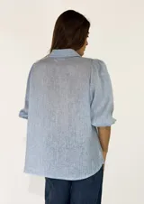 Camisa de lino color celeste, con cuello camisero, cierre frontal con botones y mangas abullonadas tres cuartos.