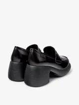 Mocasín de piel vacuna color negro, con suela de plataforma y tacón grueso. Presenta un diseño clásico con antifaz en el empeine y logo de la marca en el talón.