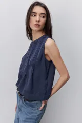 Blusa sin mangas color negro, de silueta fluida, con cuello redondo, detalle de alforzas en el frente y abotonadura parcial con botones visibles.