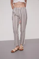 Pantalón babucha a rayas verticales grises y blancas, con cintura elástica y cordón ajustable con borlas decorativas.