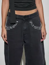 Bermuda de denim negro con tiro medio, bolsillos frontales decorados con strass y apliques de pedrería, y terminación desmechada en las piernas.