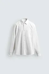 Camisa de corte regular fit confeccionada en tejido de algodón con textura. Presenta cuello solapa, cierre frontal de botones, manga larga con puño abotonado y un bolsillo plastrón en el pecho.