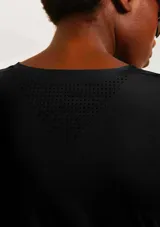 Camiseta deportiva de manga corta en color negro, confeccionada en tejido técnico transpirable con detalles de perforaciones laterales para mayor ventilación. Presenta un corte ajustado y logo reflectante en el ruedo.