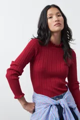 Polera de tejido acanalado con cuello alto y puños con terminación de volados. Presenta una silueta entallada y textura vertical que estiliza la figura.