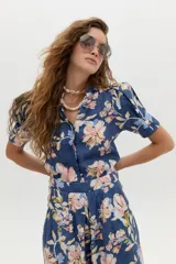 Camisa de lino azul con estampado floral en tonos rosados y beige, cuello mao con escote en V y mangas cortas abullonadas.