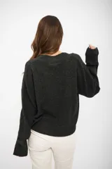 Buzo de punto color gris oscuro, con escote en V, manga larga y hombros caídos. Presenta un diseño holgado con terminaciones acanaladas en puños y ruedo.