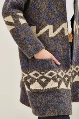 Tapado tipo cárdigan de tejido de punto con diseño geométrico en tonos azul, gris y crudo. Presenta un corte holgado, mangas largas y bolsillos laterales frontales.