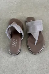 Ojota plana de cuero vacuno color marrón, de diseño tipo dedo con tira ancha en el empeine y detalle de aplique metálico con el logo de la marca.
