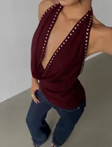 Top halter color bordó con escote profundo drapeado, espalda descubierta y detalles de tachas metálicas en los bordes.
