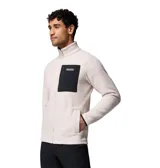 Campera de polar tipo sherpa en color beige, con cierre frontal completo y cuello alto. Presenta un bolsillo frontal en el pecho con cierre y revestimiento en contraste negro, además de bolsillos laterales. Incluye el logo de la marca en el bolsillo del pecho.