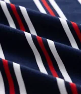 Remera polo de algodón con diseño a rayas horizontales en azul marino, rojo y blanco, corte boxy amplio, mangas cortas y cuello polo con botones. Presenta un pequeño bordado en el pecho.