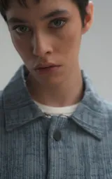 Campera de denim rígido con textura de trama única, corte oversize, cuello camisero, cierre frontal con botones y bolsillos delanteros con solapa.