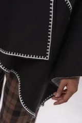 Ruana negra de corte asimétrico con detalles de costura a contraste en color blanco en los bordes. Confeccionada en tejido de algodón, presenta una caída fluida y diseño abierto.