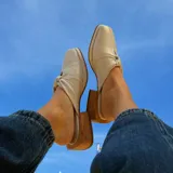 Zueco de cuero vacuno color beige con detalle de nudo en el empeine, punta cuadrada y taco bajo de madera.