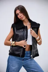 Chaleco de cuero sintético con acabado gamuzado, forrado en corderito negro. Presenta cierre frontal, cuello solapa, detalles de correas ajustables en los laterales y ribetes de corderito en los bordes.