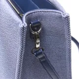 Cartera grande tipo tote bag de textura denim con detalles en cuero sintético azul oscuro. Cuenta con doble asa de mano, correa ajustable para el hombro y un bolsillo frontal con cierre y el logo de la marca Extra Large.