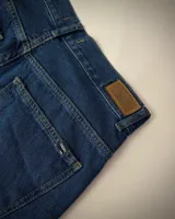 Short de jean de mezclilla azul oscuro, corte ancho y largo (tipo bermuda), con bordes deshilachados y dobladillo sin rematar.