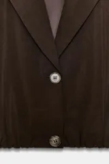 Blazer corto de color marrón oscuro, con cuello solapa, cierre frontal de botones y mangas largas con puños vueltos. Presenta un diseño con bajo elástico que le otorga una silueta ajustada en la cintura.