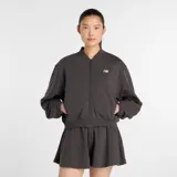 Campera tipo bomber de New Balance, color gris oscuro, con cierre frontal completo, cuello, puños y ruedo acanalados. Presenta bolsillos laterales y el logo de la marca bordado en el pecho.