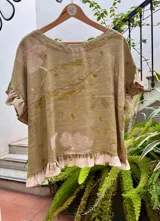 Top de lino con estampado botánico artesanal (ecoprint) en tonos verdes y beige. Presenta un corte holgado, mangas cortas con volados y un volado en el ruedo inferior.